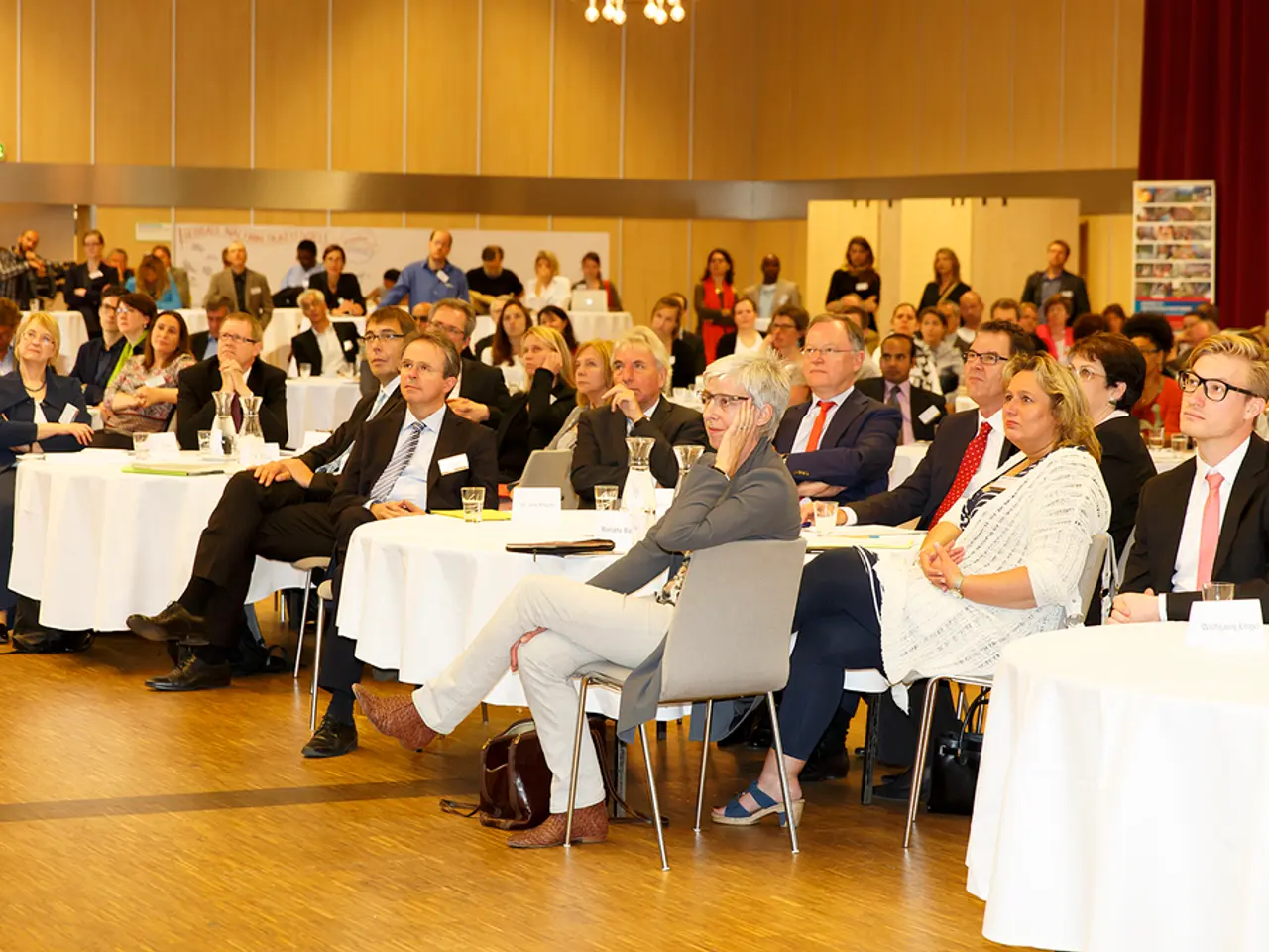 People are sitting in groups at tables and listening to something.