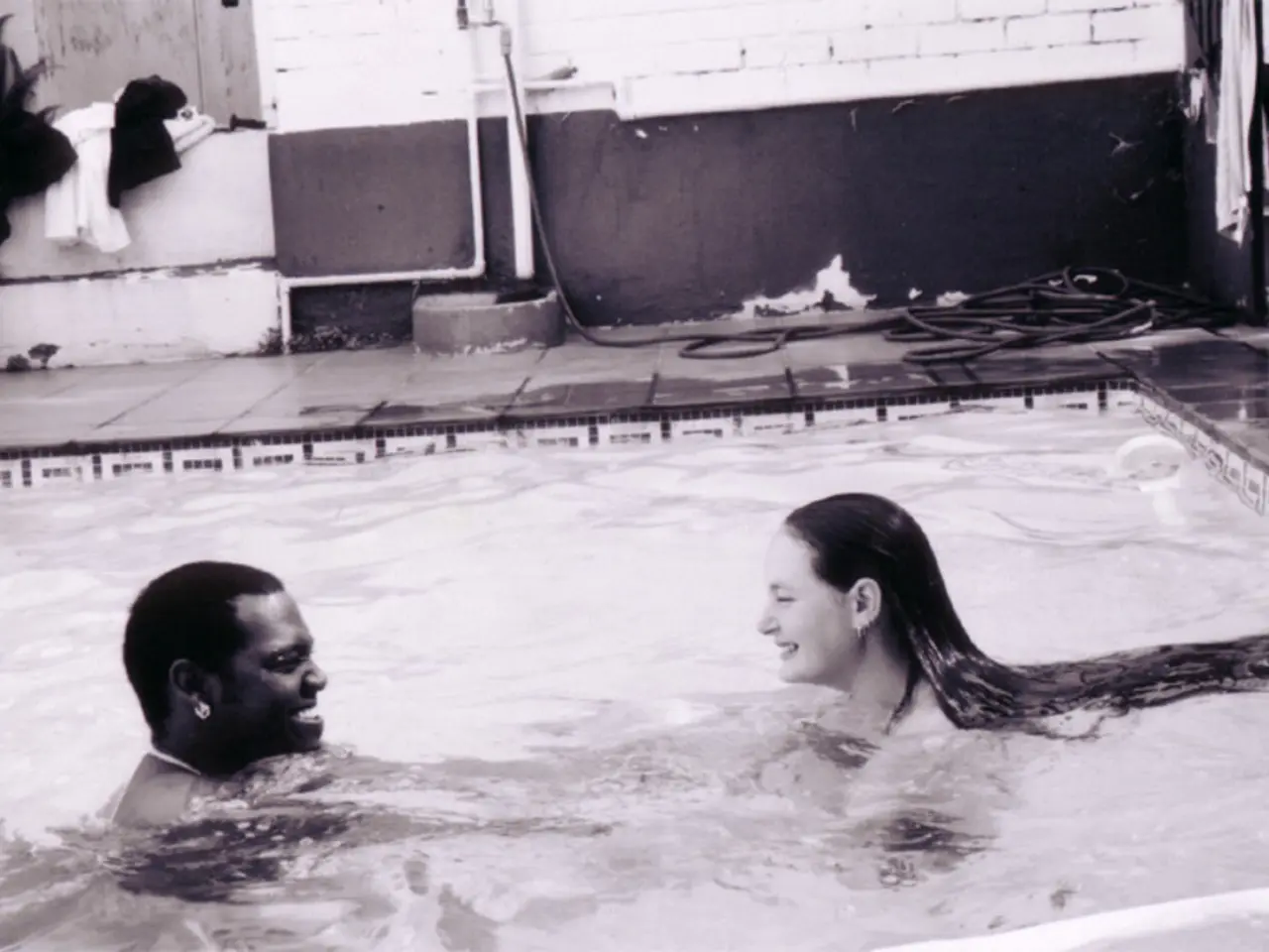 In the foreground of the picture there is swimming pool, in the pool there are two persons...