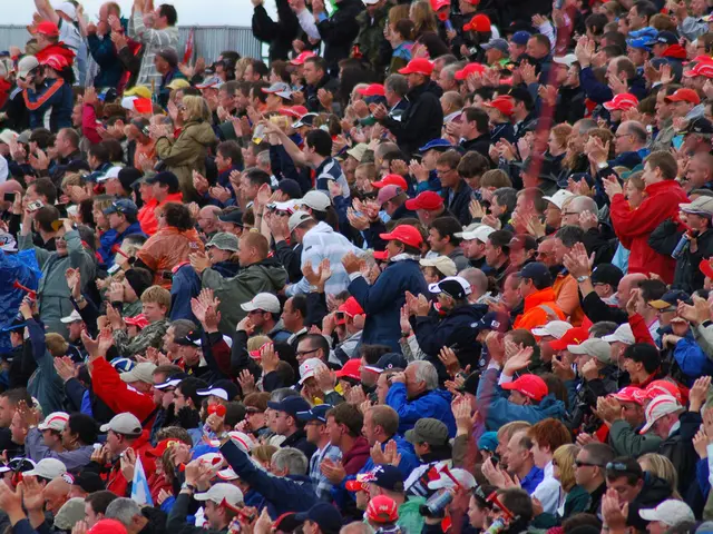 This image consists of a huge crowd. Most of them are wearing red caps. In the background, it looks...