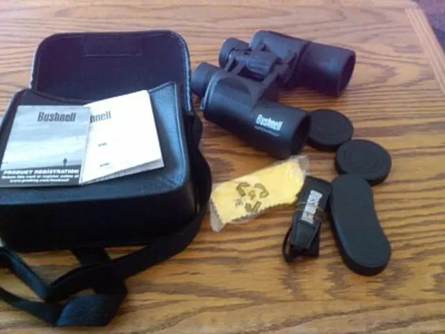 In this picture we can see a bag, papers, binoculars and other things on the wooden plank.