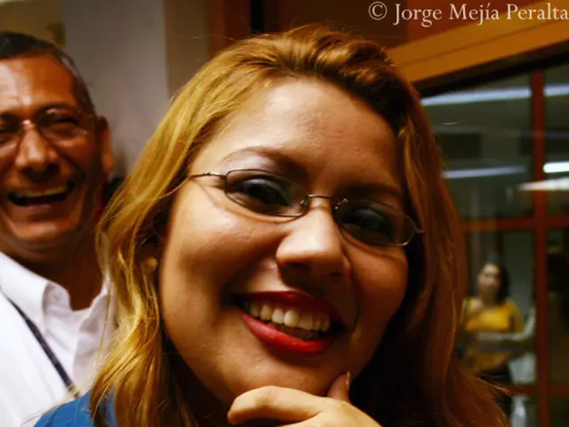 In this image we can see people smiling. In the background there is a wall and a door.