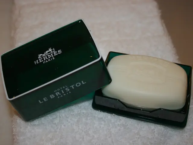 In the image there on the cloth there is a box with a soap. Beside that there is a box lid with...