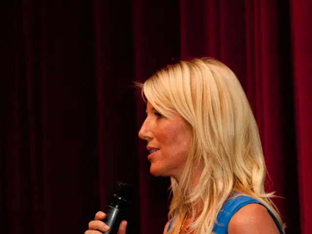 In the image we see there is a woman who is standing and in her hand there is mike, water bottle...