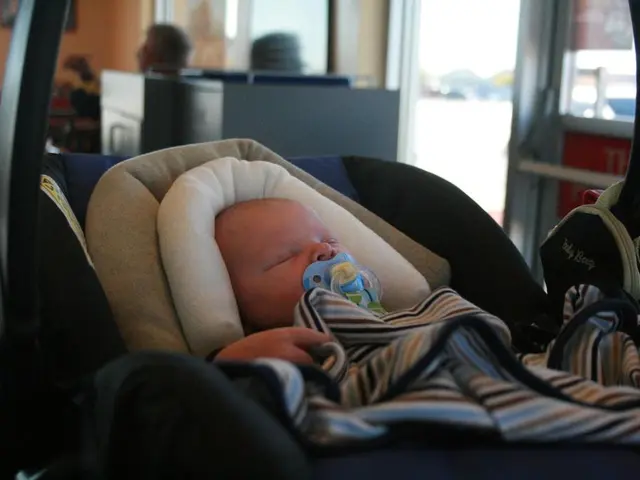 In this image we can see a baby with a soother in the mouth. And the baby is lying on a stroller....