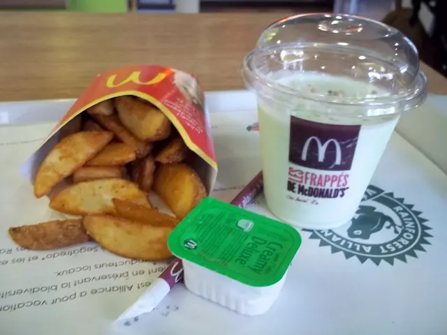 There is a table in the image, there is a milkshake, it seems like chips, straw and a small cream...