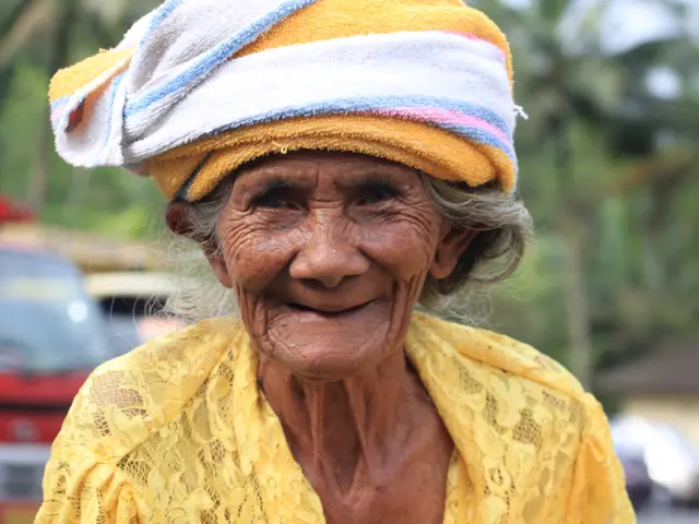 Here I can see an old lady wearing a yellow color dress and headband and smiling. On the left side,...