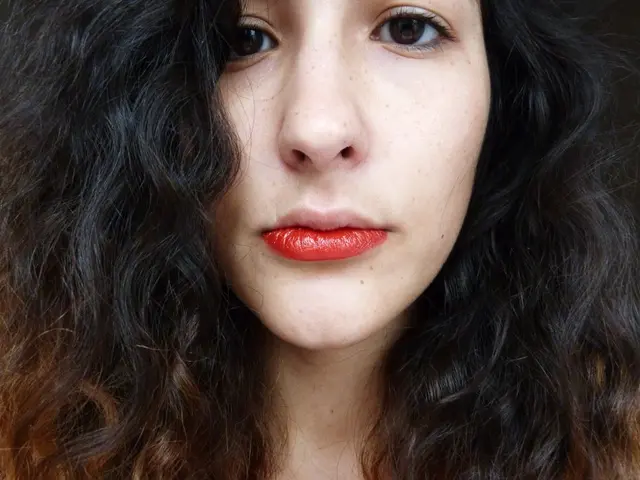 In this image I can see a woman is looking at this side, she wore red color lipstick.